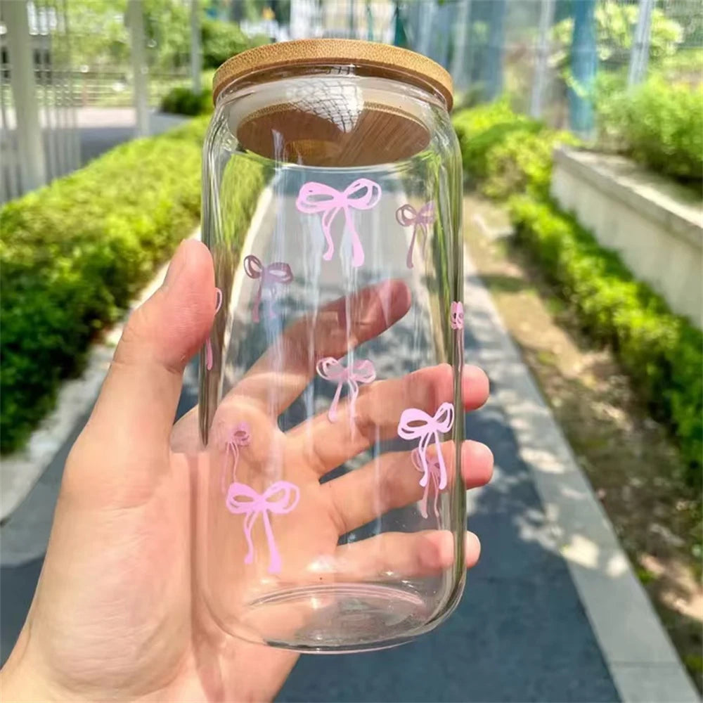 Clear glass jar with pink bow designs and a wooden lid, held in a hand outdoors.