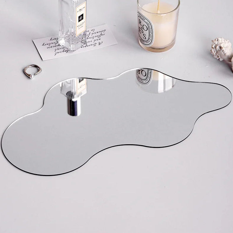 Decorative mirror with a unique shape on a light gray surface with a candle and perfume bottle.