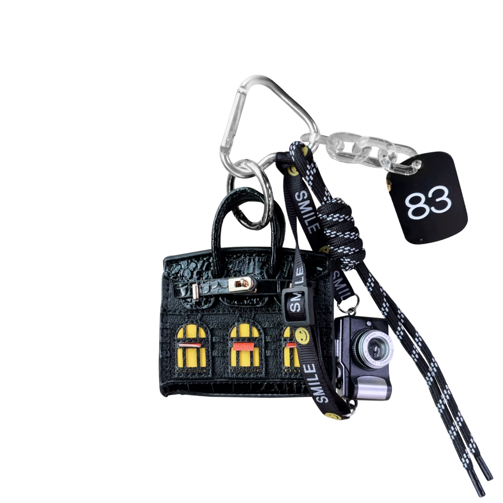 Black leather structured mini bag charm shaped like a house, featuring decorative window panels and a top handle.