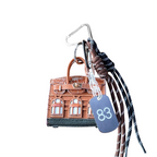 Brown leather structured mini bag charm shaped like a house, featuring decorative window panels and a top handle.