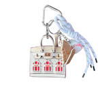 White leather structured mini bag charm shaped like a house, featuring decorative window panels and a top handle.