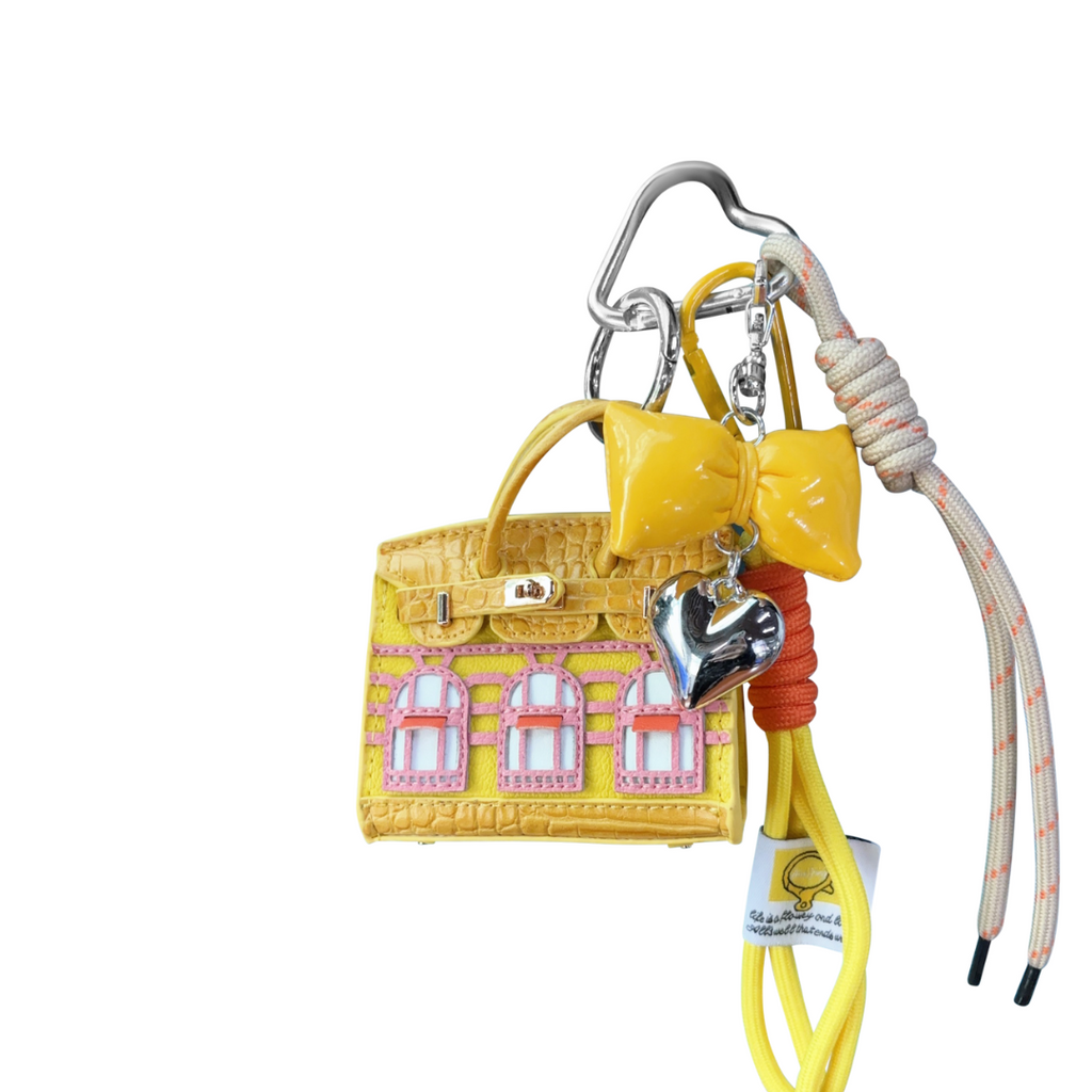 Yellow leather structured mini bag charm shaped like a house, featuring decorative window panels and a top handle.