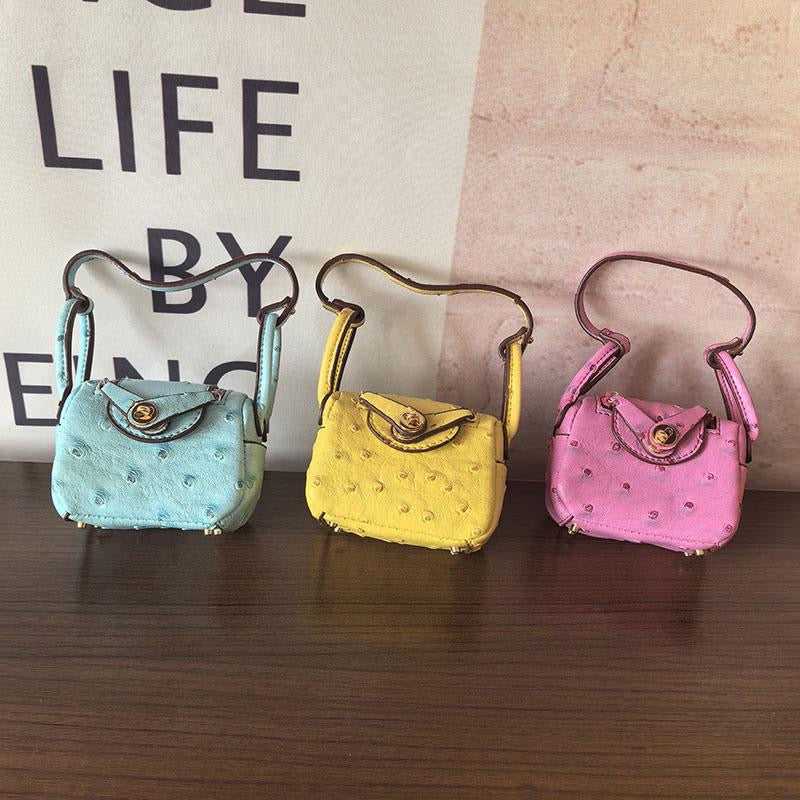 Three small mini handbags charms in blue, yellow, and pink on a wooden surface with a blurred background.