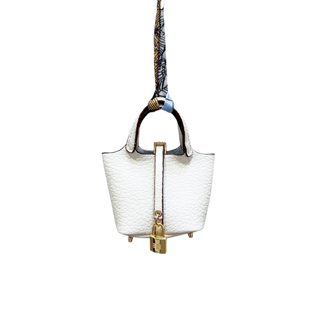 A white leaWhite leather mini bucket bag charm with gold padlock detail, structured sides, and open-top storage functionality.ther picnic tote bag charm with a metallic clasp and a brown leather handle.