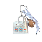 White structured mini bag charm shaped like a house, featuring decorative window panels and a top handle.