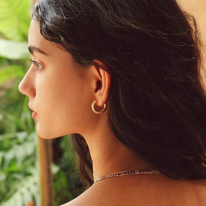 Woman wearing gold hoop earrings with a blurred green background