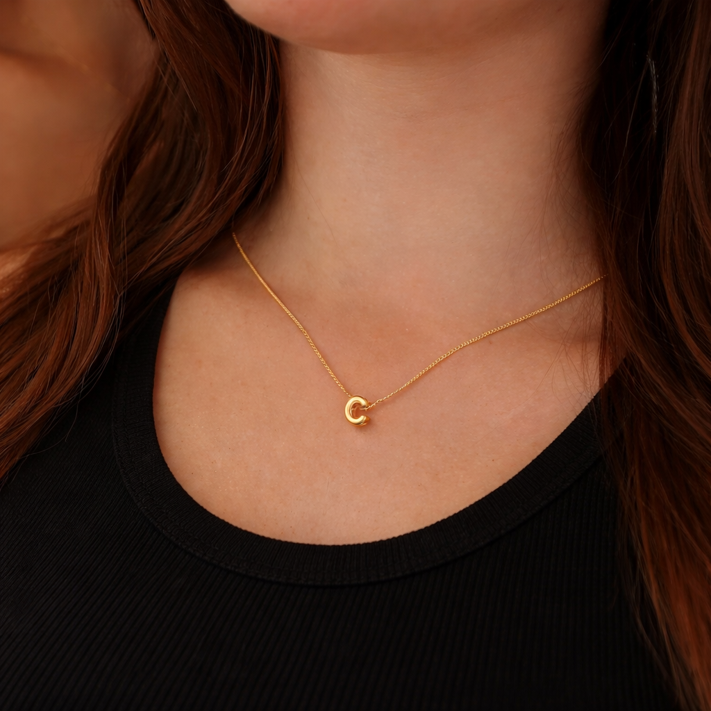 Gold necklace with a small round pendant on a person wearing a black top.