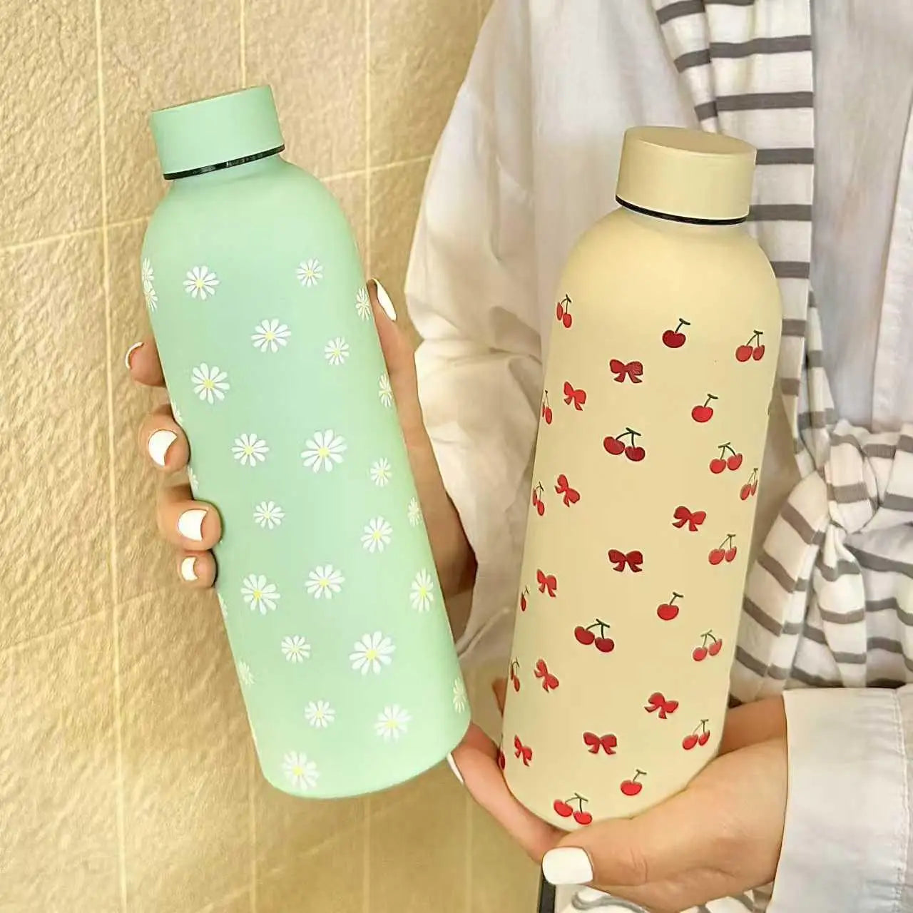 Two water bottles with floral and cherry designs held by a person.