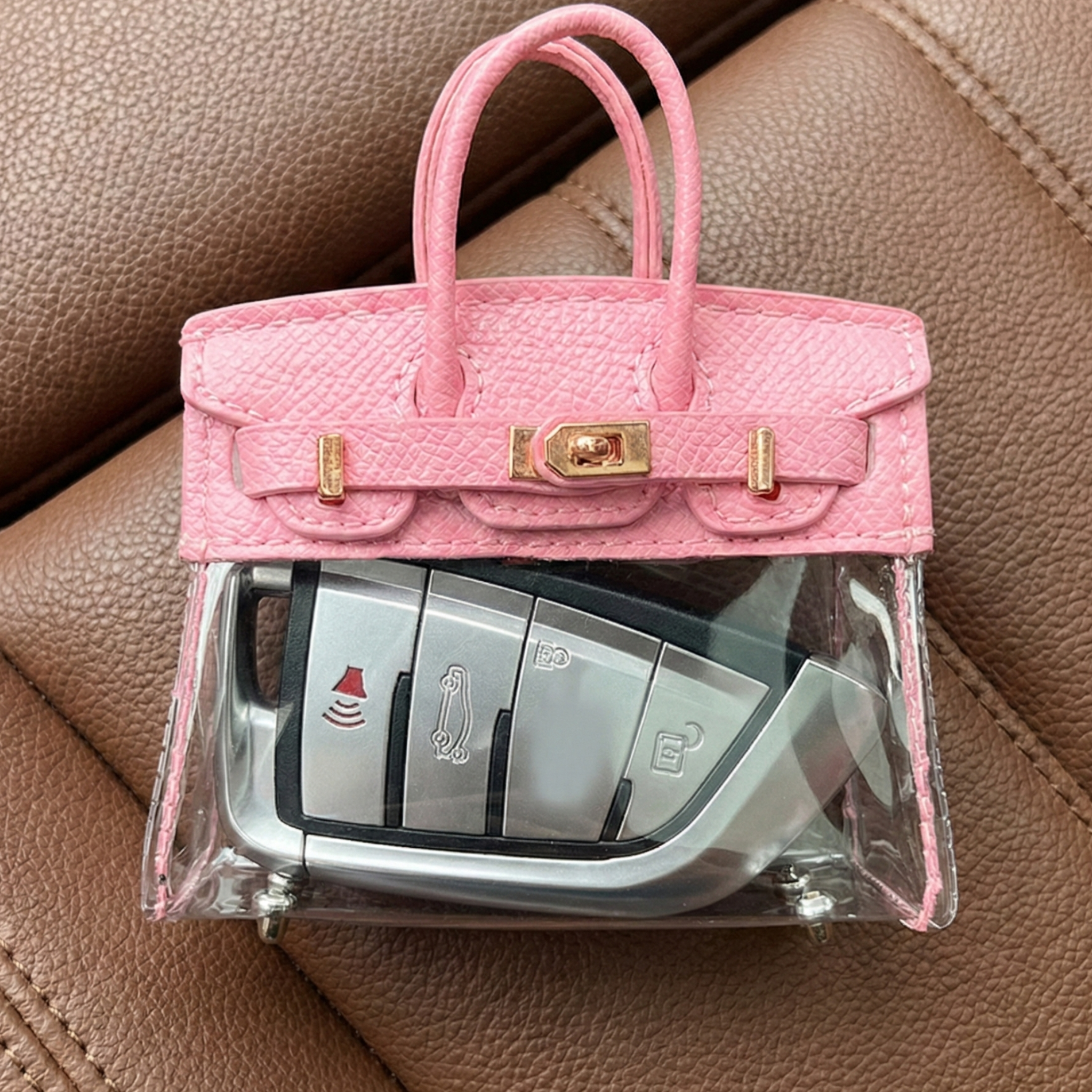 Pink handbag with a clear cover holding car keys on a brown leather surface