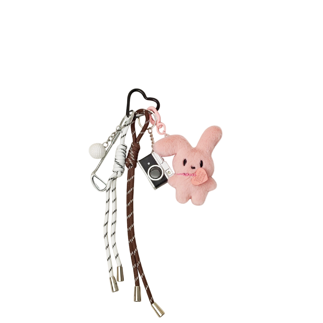 White and pink plush bunny head bag charm with a miniature camera, golf ball, and golf club components hanging from a keychain.