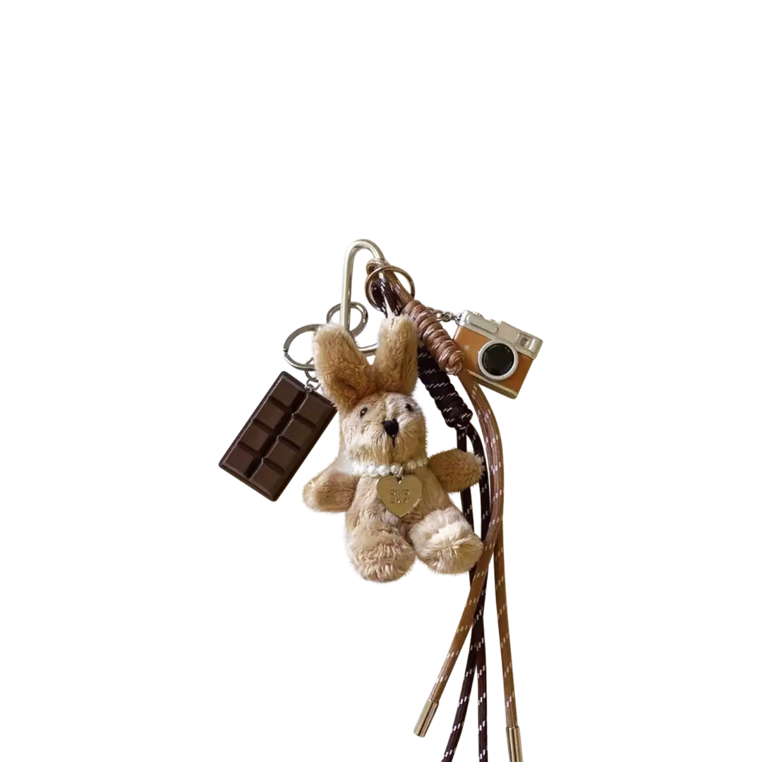Beige plush bunny bag charm with miniature chocolate bar and vintage camera components hanging from a keychain.