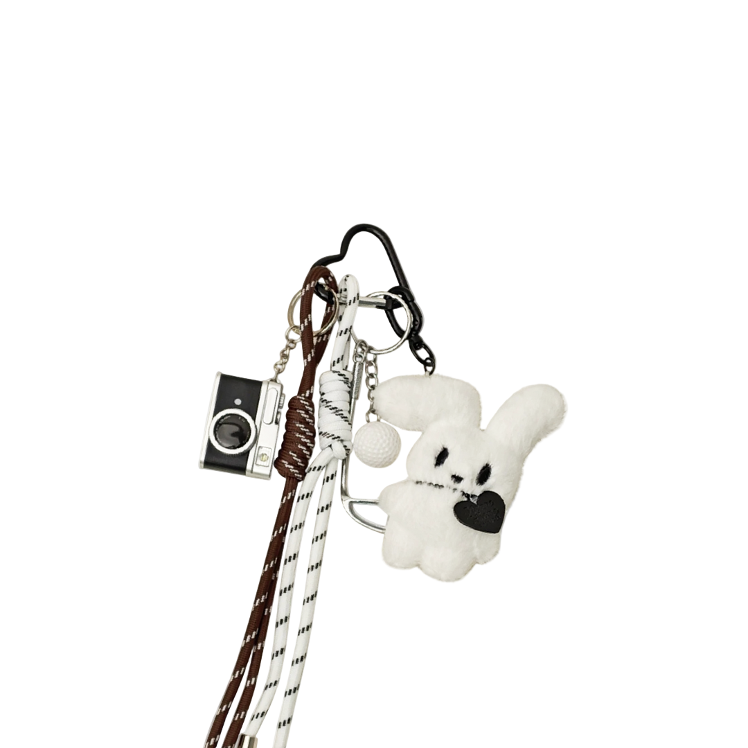 White plush bunny bag charm with a black heart patch, brown accents, and keychain featuring a camera, golf ball, and golf club components.
