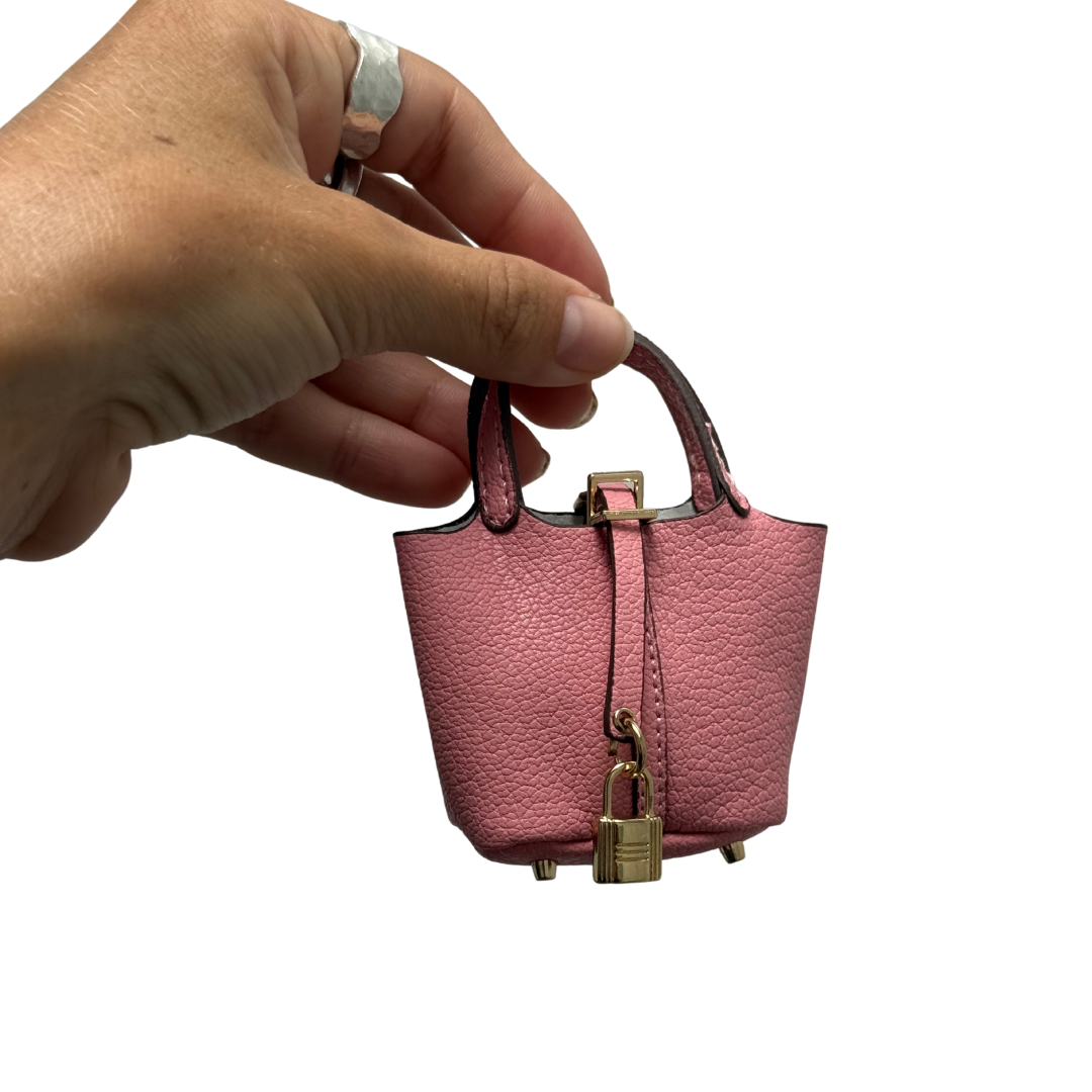 Close-up of a hand holding a pink padlock bucket bag charm, highlighting its textured leather, gold padlock, and miniature size.