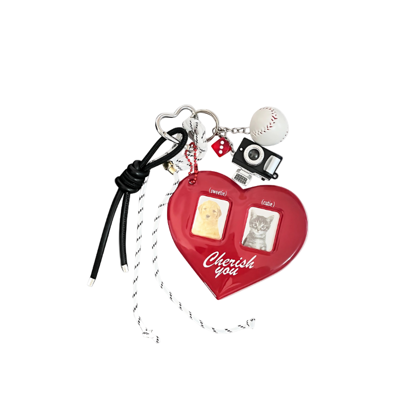 Large red heart-shaped locket charm with a clear photo frame center, paired with a silver camera charm, dice, and baseball components hanging from a keychain.