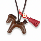 Brown horse-shaped keychain with a red tassel on a white background