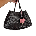 Black woven handbag with a pink mini bag charm attached to it on a white background