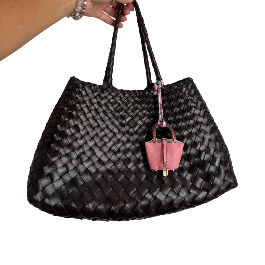 Black woven handbag with a pink mini bag charm attached to it on a white background