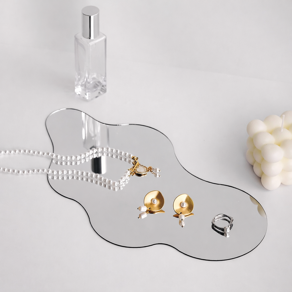 Jewelry on a mirrored tray with a perfume bottle and decorative item on a light gray background