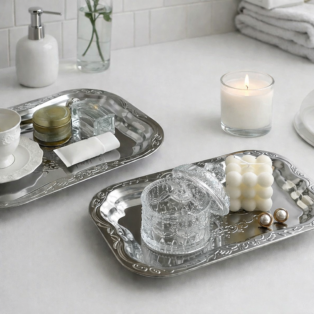 Two silver trays on a bathroom counter with various items including candles and soap.