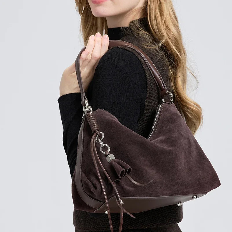 Brown suede handbag held by a person against a light gray background